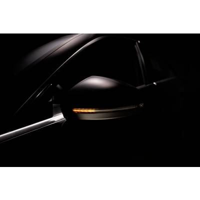 Gros plan sur un rétroviseur de voiture avec un clignotant allumé dans un environnement sombre. L'accent est mis sur le clignotant lumineux.
