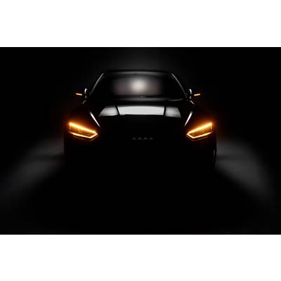 'Voiture sombre avec un phare avant orange allumé, prise de face, se détachant sur un fond noir.'