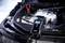 Un chargeur de batterie est connecté à une batterie de voiture et affiche '14,2V' sur un écran. Les bornes de la batterie sont visibles.