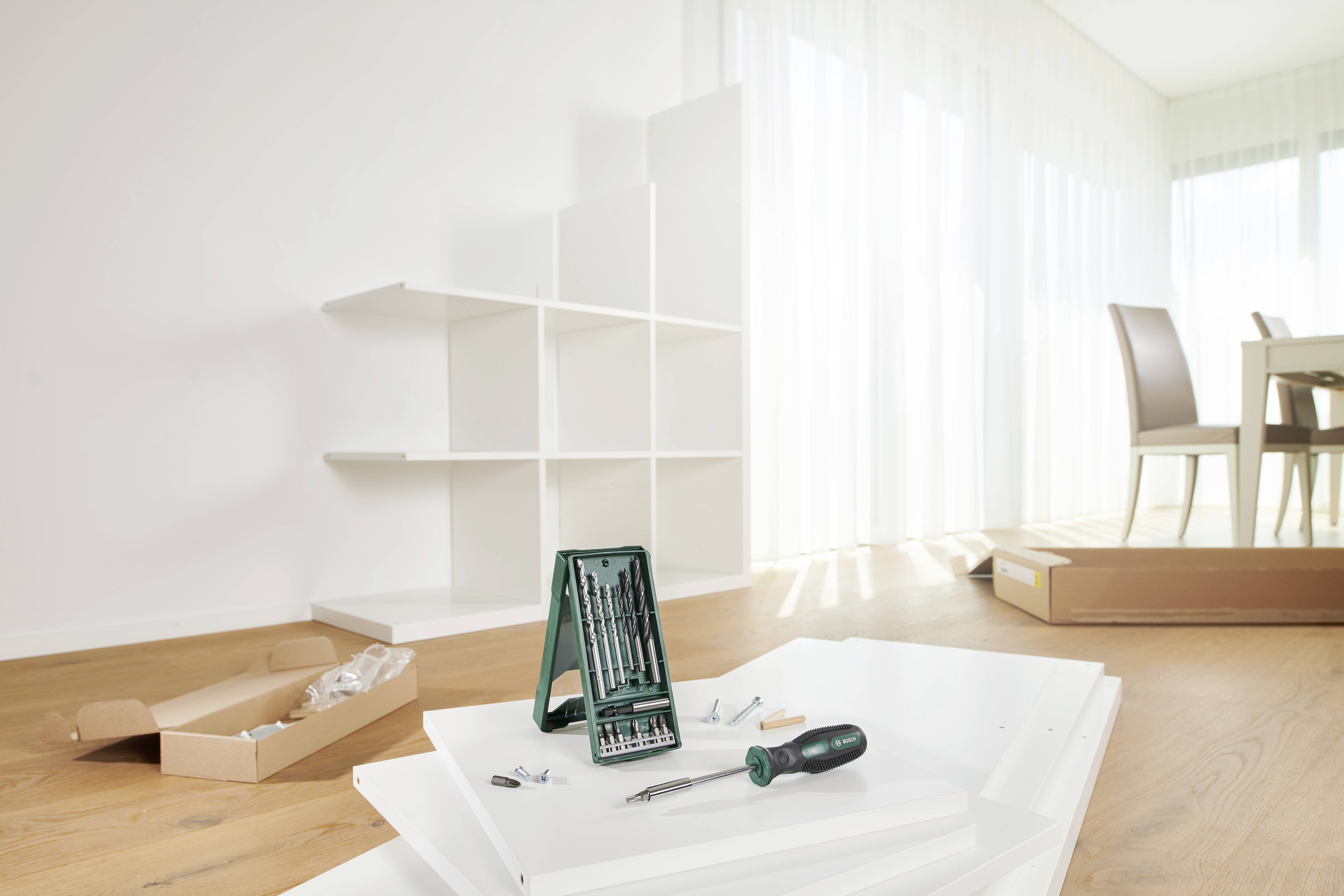 Une étagère blanche partiellement assemblée, avec des outils et des vis sur le sol, dans une pièce moderne et lumineuse à côté d'une table à manger.