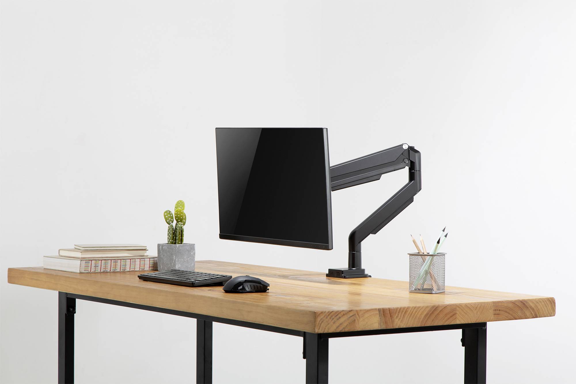 Un bureau moderne et bien rangé avec un bras de support de moniteur, un écran, un clavier, une souris, une plante de cactus, une pile de livres et un porte-stylos.