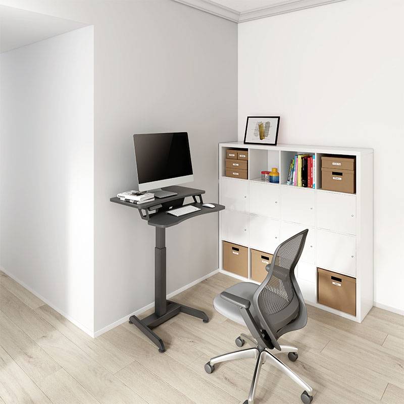 Bureau réglable en hauteur avec un ordinateur portable et un cahier, à côté d'une chaise et d'une étagère avec des boîtes de rangement dans un bureau moderne.