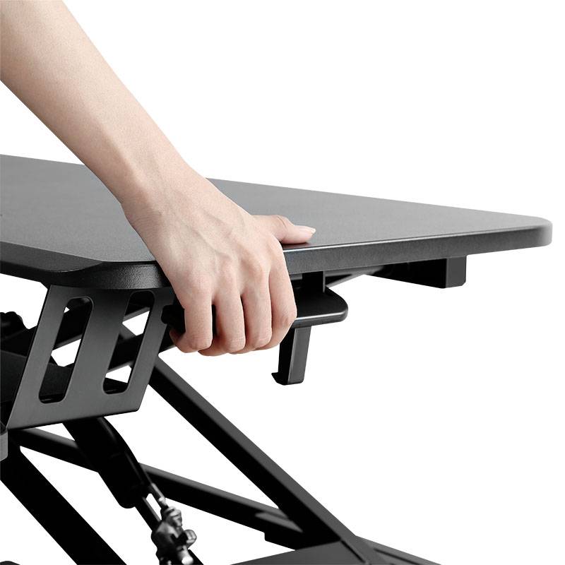 Une main soulève une table réglable en hauteur. La table est noire et présente un design moderne.