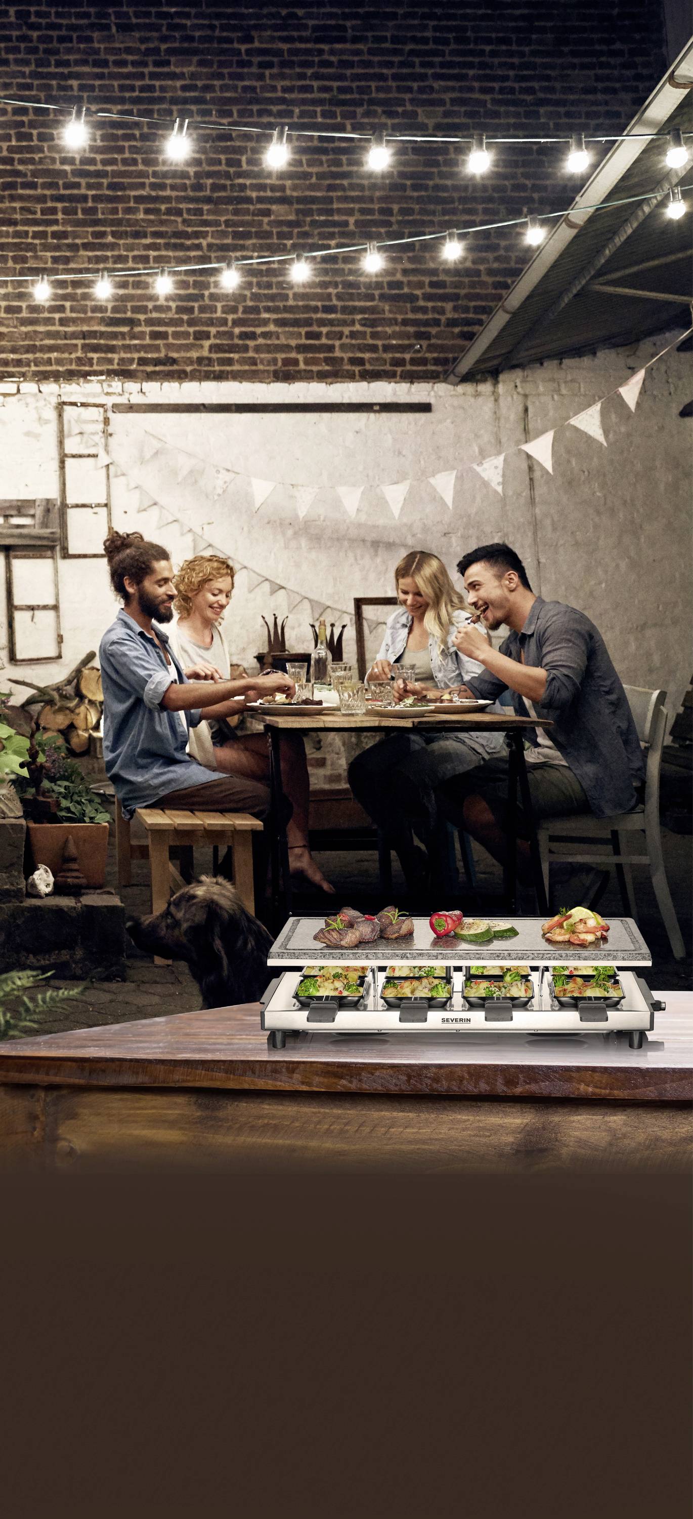 Quatre personnes sont attablées en extérieur sous des guirlandes lumineuses. Au premier plan, un barbecue est chargé de légumes et de viande.