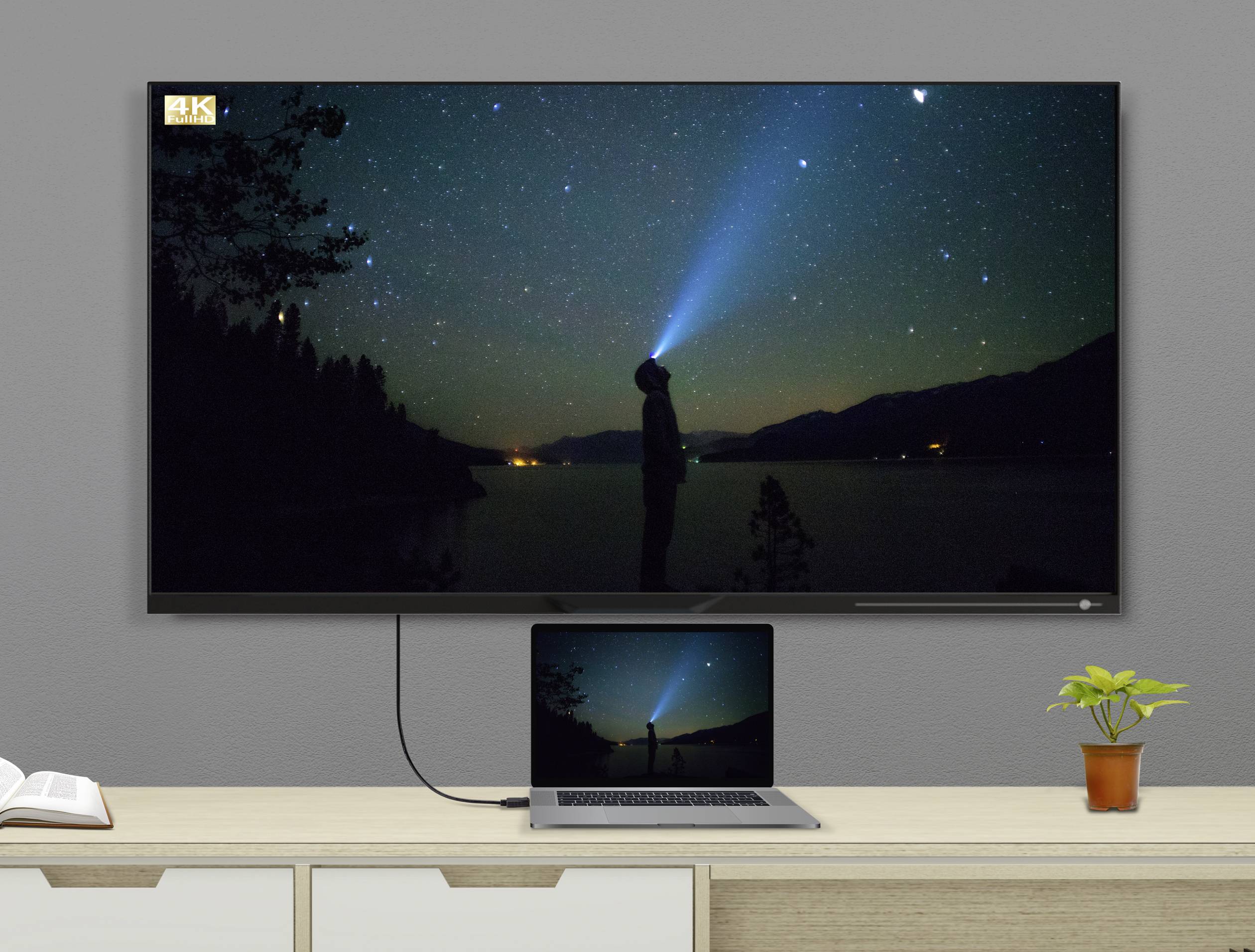 Un ordinateur portable posé sur une table est connecté à un grand écran de télévision fixé au mur, sur lequel on peut voir l'image d'un ciel nocturne étoilé avec une personne tenant une lampe de poche.