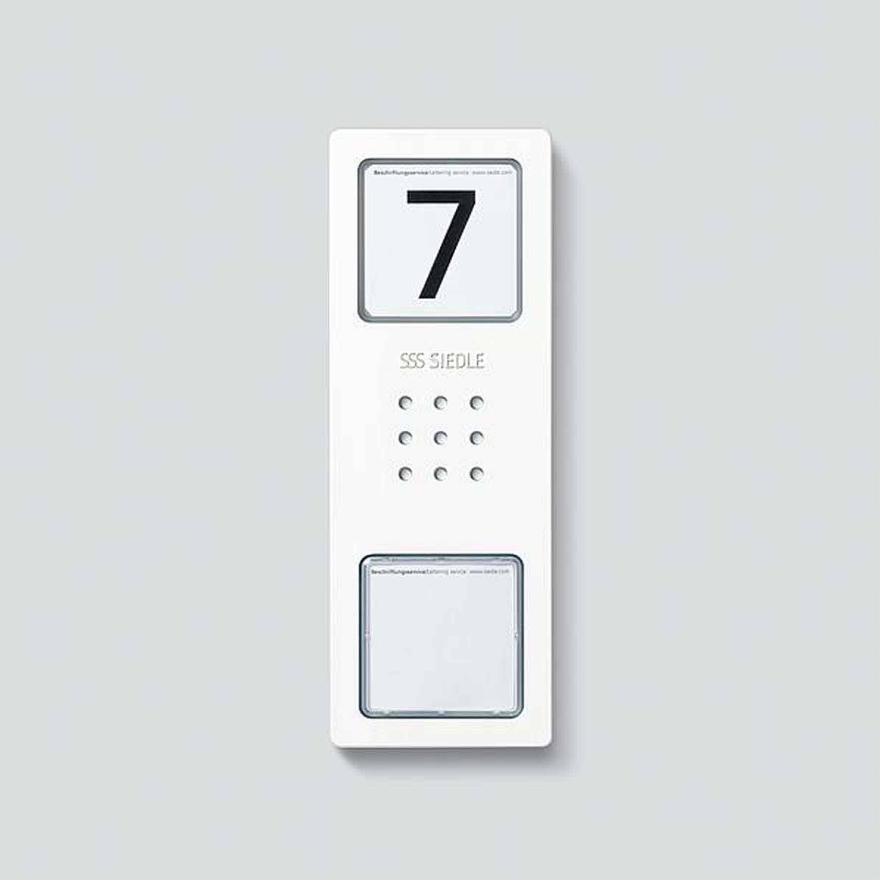 Interphone avec le numéro '7', microphone et haut-parleur au centre, affichage lumineux en haut et plaque nominative en bas.