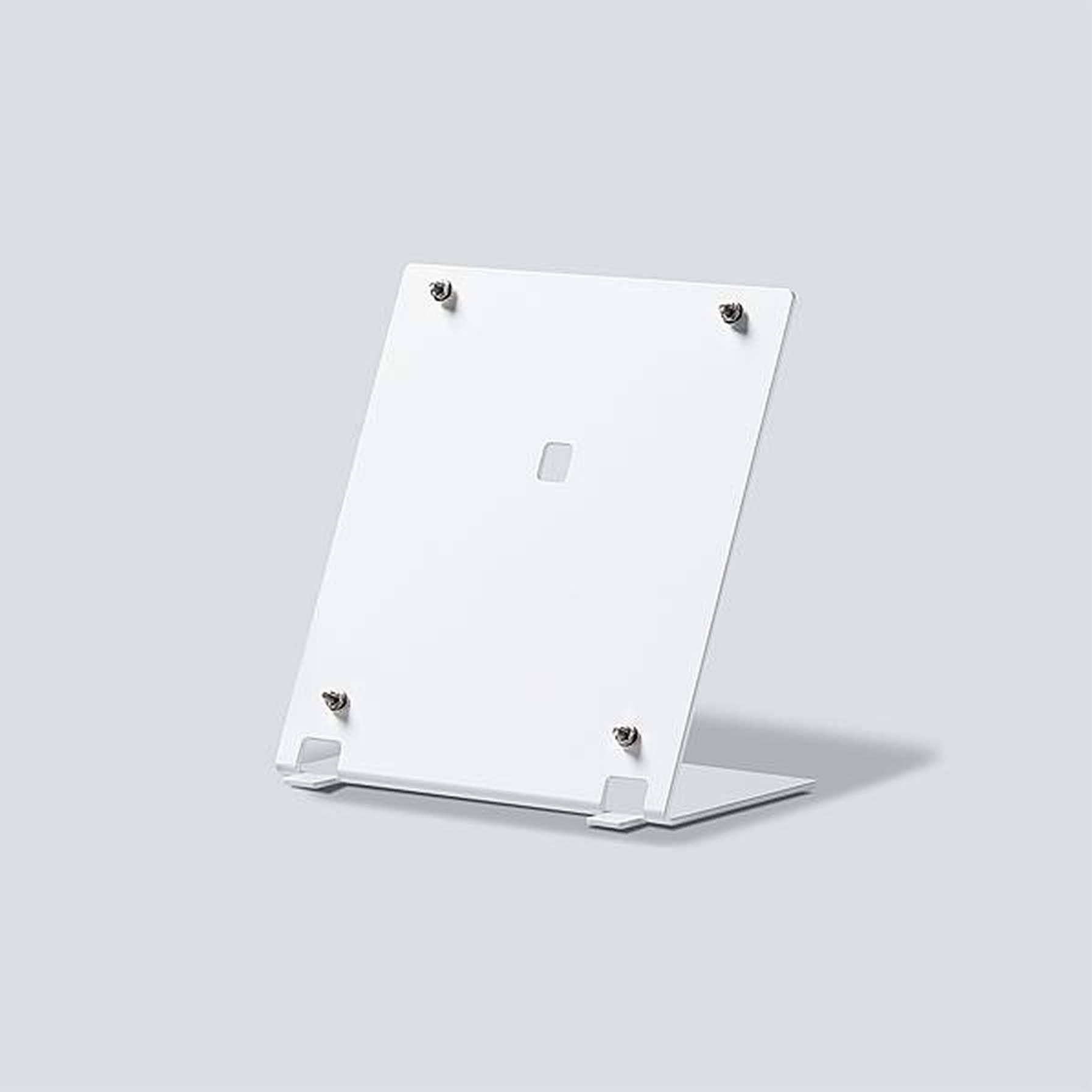 Une plaque métallique blanche rectangulaire sur un support, fixée par quatre vis dans les coins, sur un fond gris.