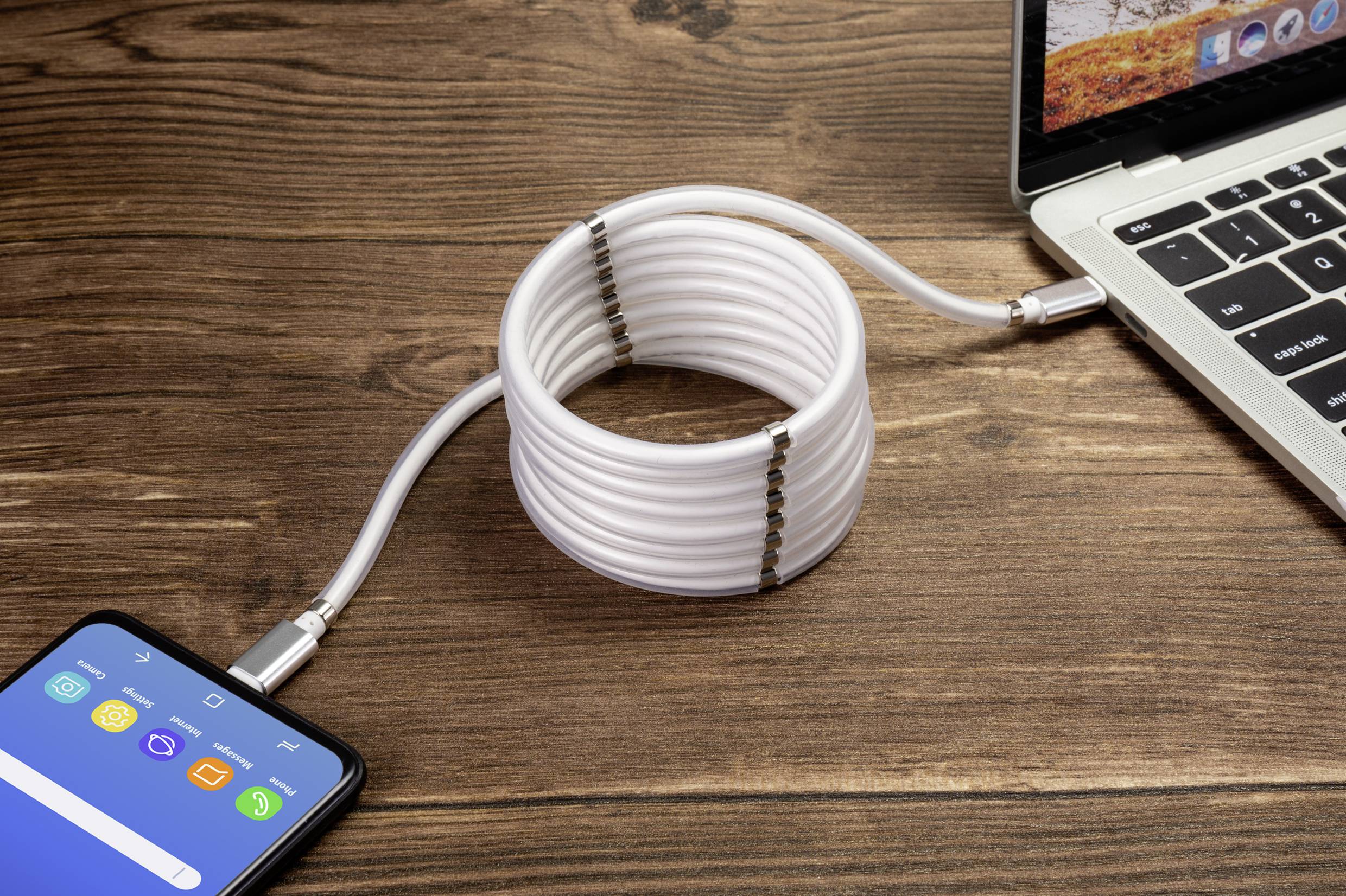 Un smartphone et un ordinateur portable sont connectés par un câble blanc spiralé sur une table en bois.