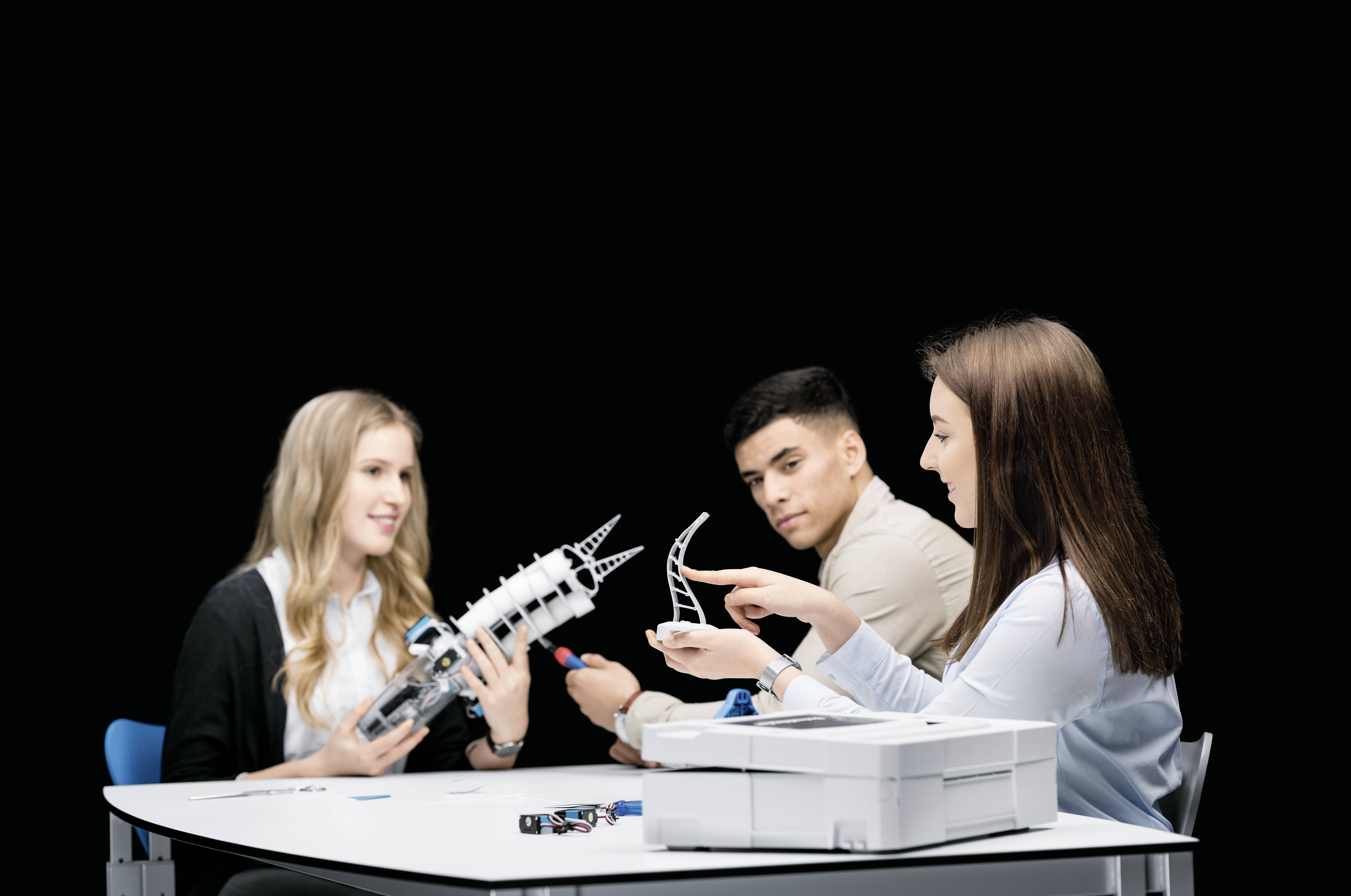 Trois jeunes adultes sont assis à une table et travaillent ensemble sur des modèles techniques.