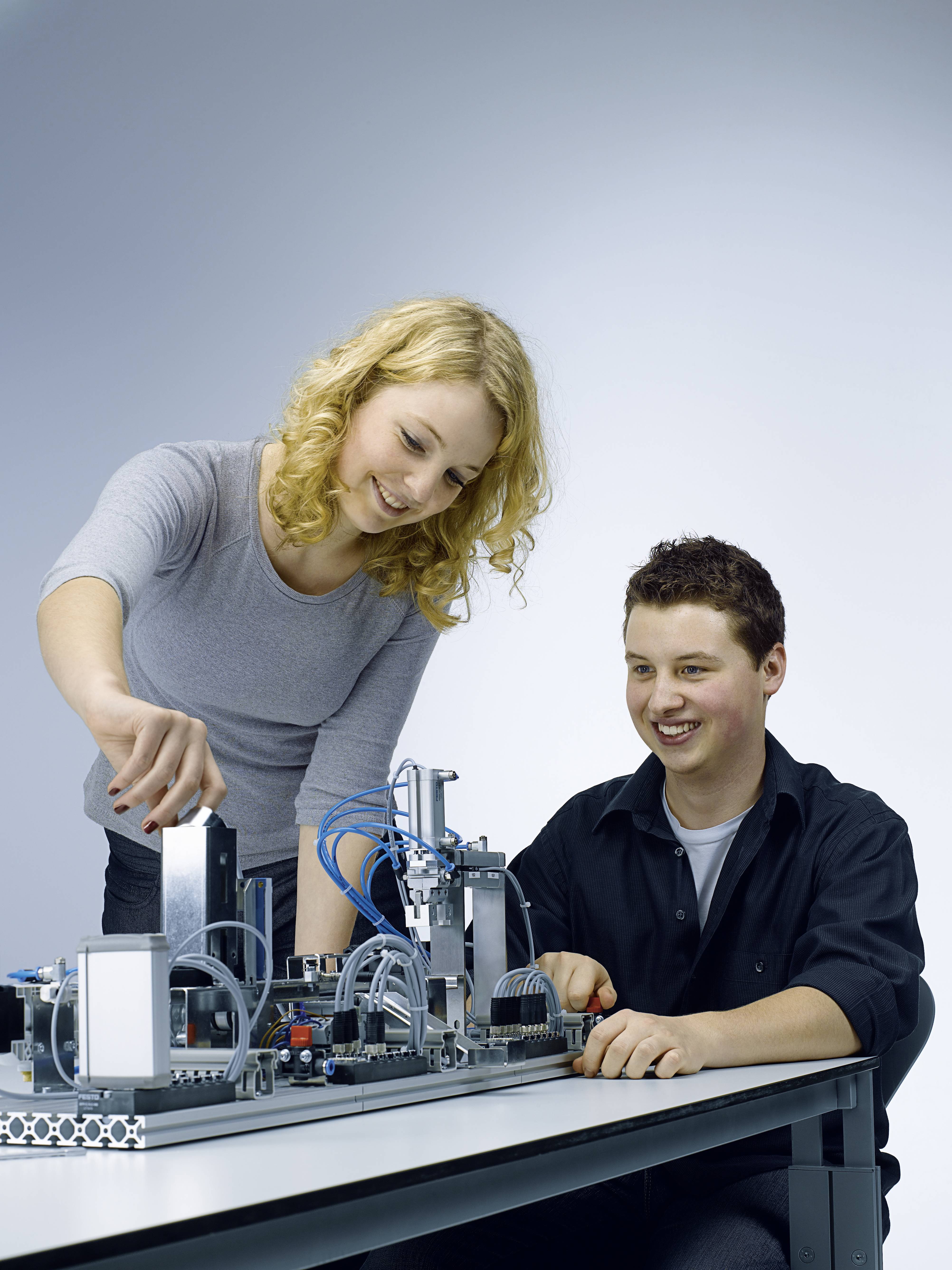 Deux personnes travaillent ensemble sur une machine technique posée sur une table. Elles sourient et sont concentrées sur leur tâche.