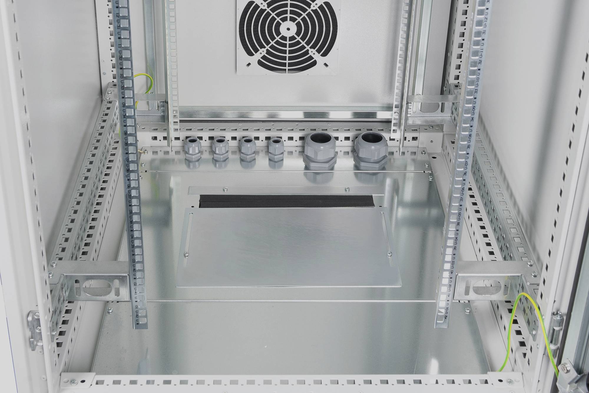 Armoire électrique vide avec ventilateur en haut au centre et ouvertures pour câbles en bas. Supports de câbles fixés sur les côtés.