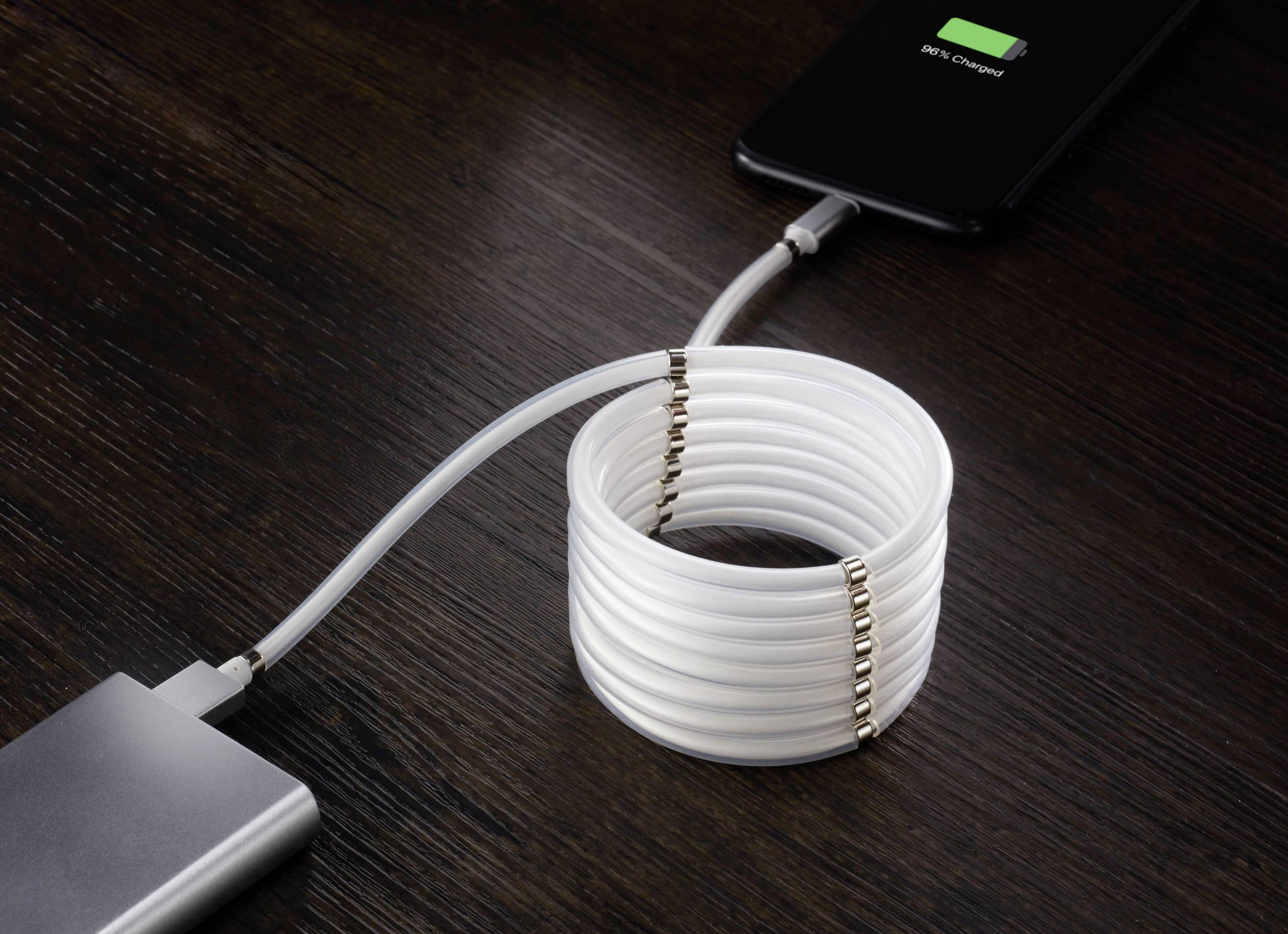 Un smartphone est en train de charger à partir d'une batterie externe avec un câble USB enroulé. Le téléphone affiche « 100% chargé ».