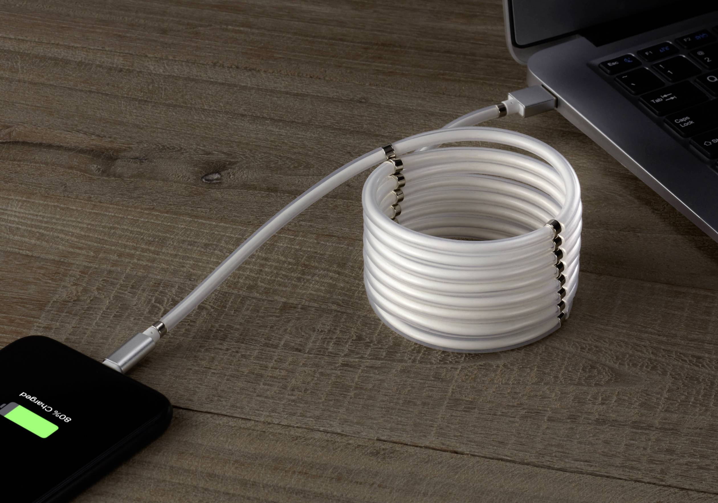 Un câble USB blanc relie un ordinateur portable à une station de charge. Le câble est artistiquement enroulé en spirale sur une table en bois.