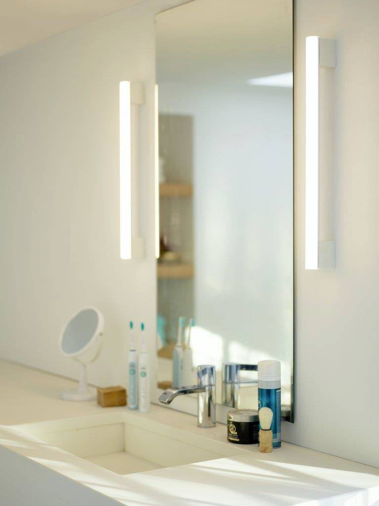 Une salle de bain moderne avec un grand miroir, à côté deux brosses à dents électriques, un distributeur de savon et des produits de soin sur un lavabo blanc.