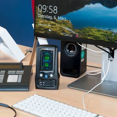 Un bureau avec un téléphone, un appareil de mesure numérique, un haut-parleur et un écran d'ordinateur affichant la date et l'heure.