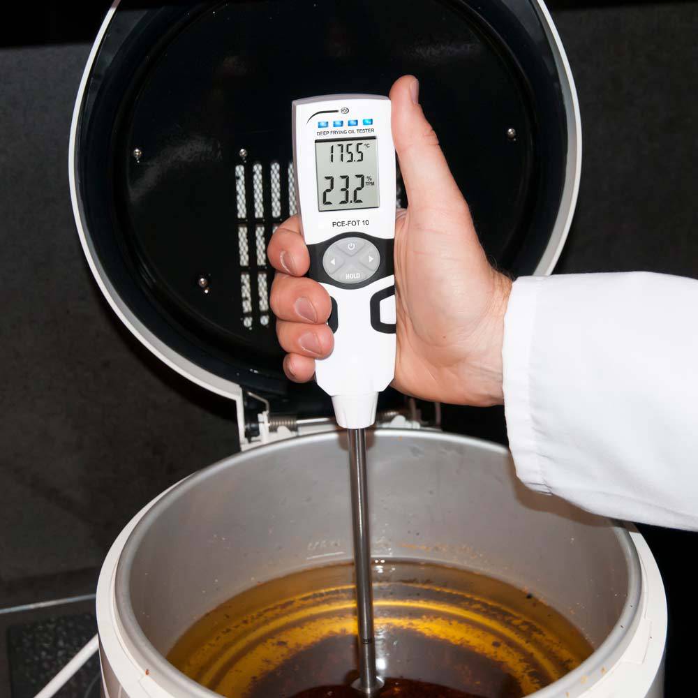 Un thermomètre est plongé dans un liquide et indique 23,2°C. Une personne portant une blouse de laboratoire blanche tient l'appareil.