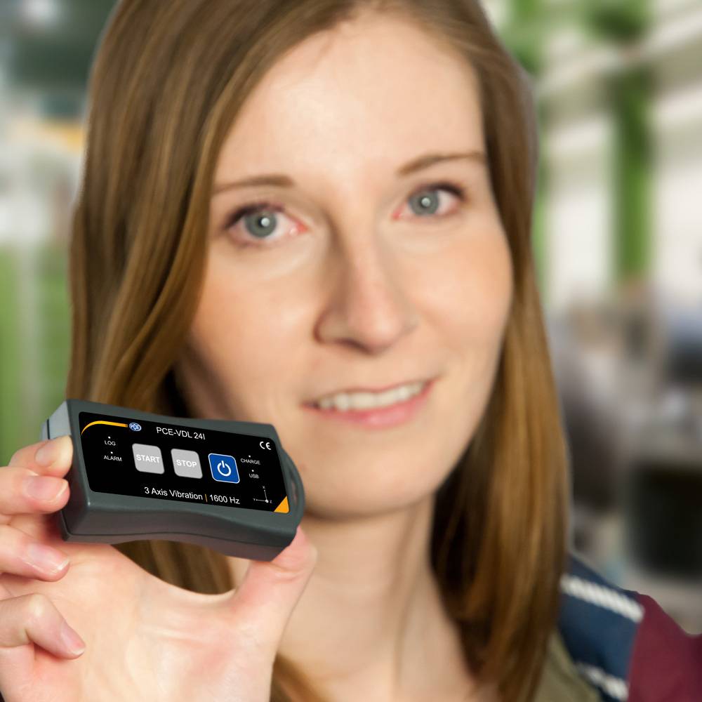 Une personne tient un appareil de mesure des vibrations dans la main. L'écran affiche des valeurs de mesure et des commandes.