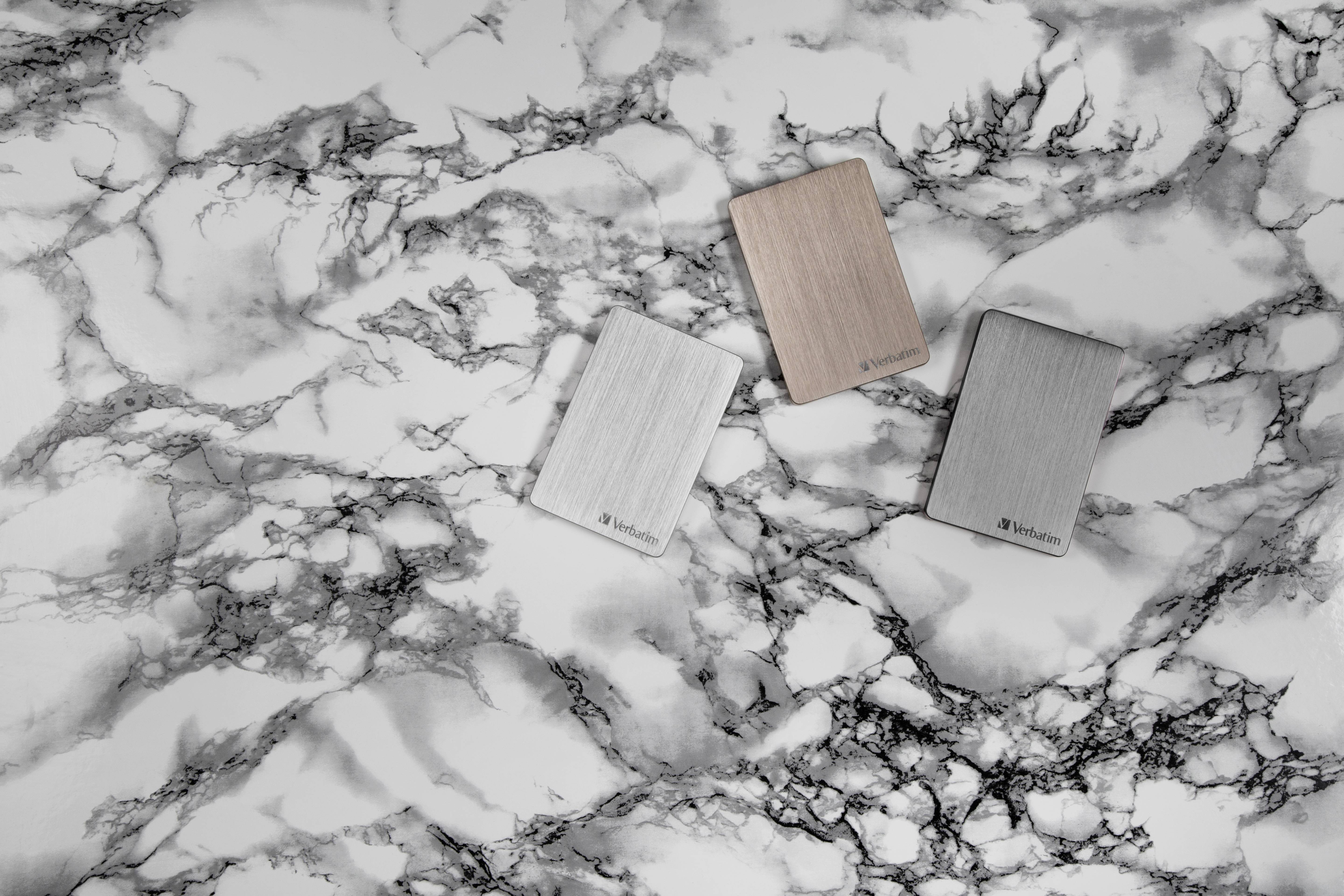 Sur une surface en marbre reposent trois disques durs externes aux couleurs argent, or rose et gris. Ils présentent un design élégant et moderne.