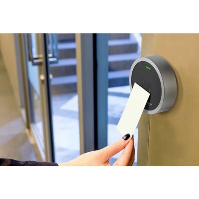 Une main tient une carte d'accès près d'un lecteur de carte moderne installé sur une porte afin d'obtenir l'accès à un bâtiment.