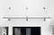 'Étagère flottante moderne avec supports métalliques fixée sur un mur blanc, au-dessus d'une porte encadrée de noir. Une œuvre d'art décorative représentant le chiffre huit est partiellement visible sur la gauche.'