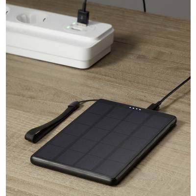 Batterie externe solaire avec indicateur de charge, posée sur une table en bois, connectée par un câble à une multiprise.