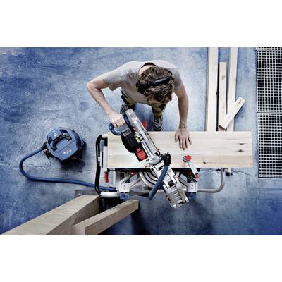 Une personne scie précisément une planche en bois à l'aide d'une scie à onglets électrique dans un environnement d'atelier.