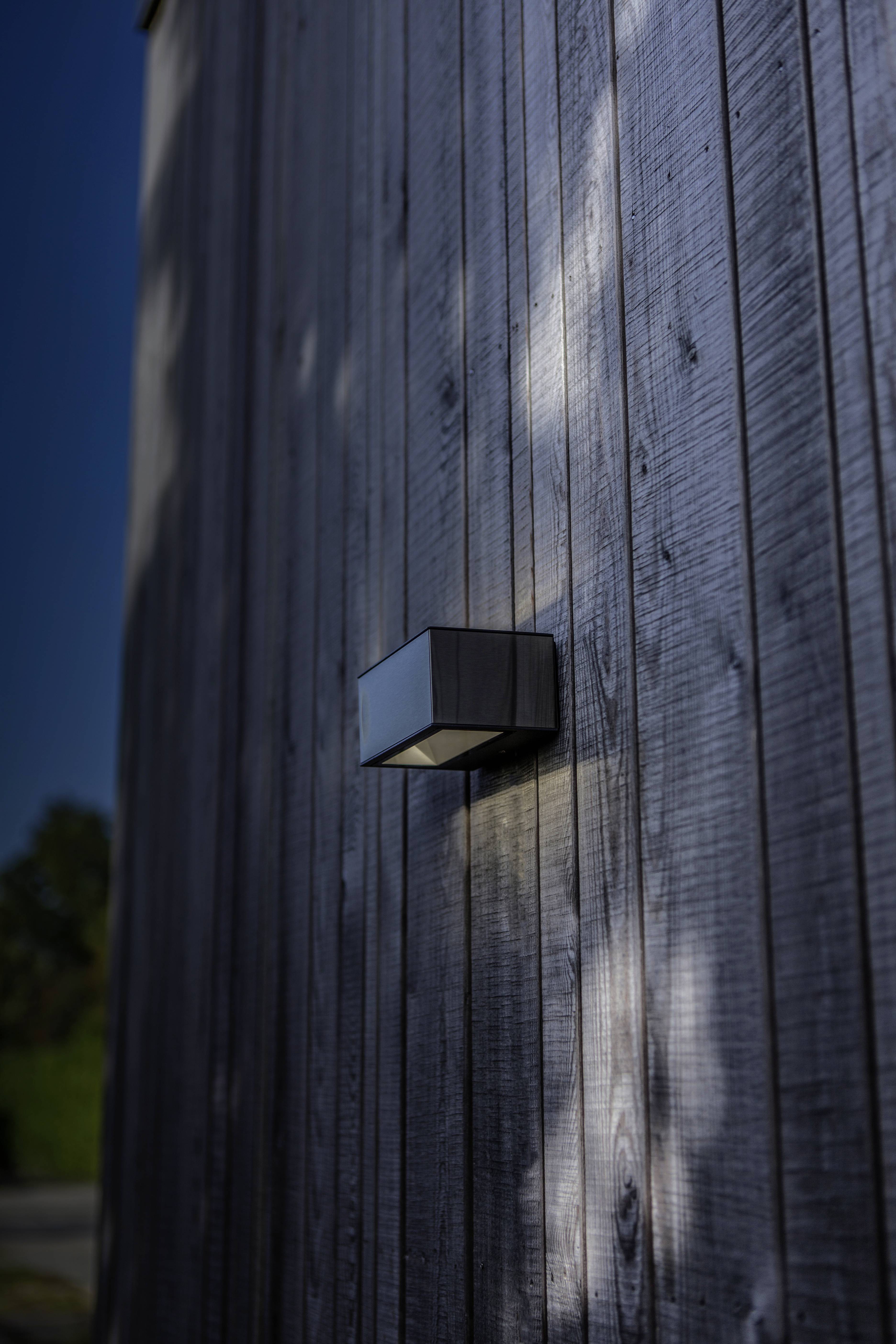 Une lampe extérieure moderne fixée à un revêtement en bois, projetant un éclairage diffus sur le mur.