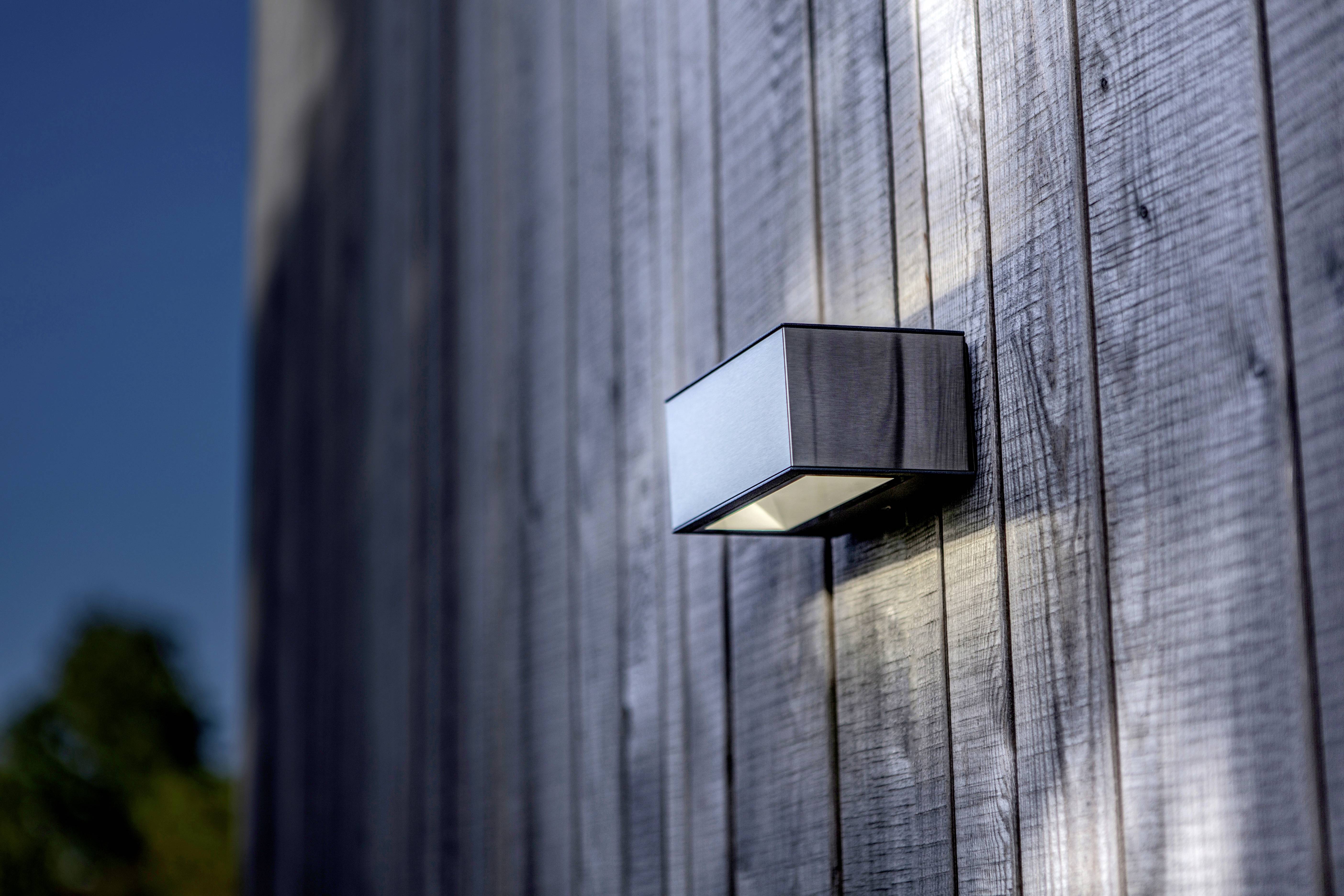 Un luminaire moderne est fixé à un mur en bois et projette sa lumière vers le bas, mettant en valeur la structure du bois.