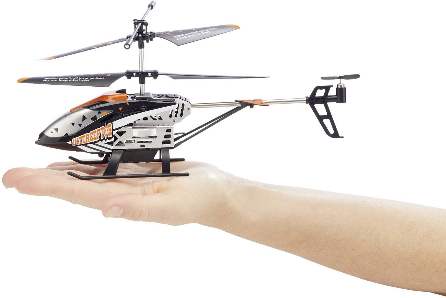 Un petit hélicoptère télécommandé est tenu dans une main. L'hélicoptère est noir, blanc et orange.