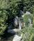 Cascade dans un jardin verdoyant, entourée de rochers, de fougères et de buissons touffus, qui se déverse dans un petit étang.