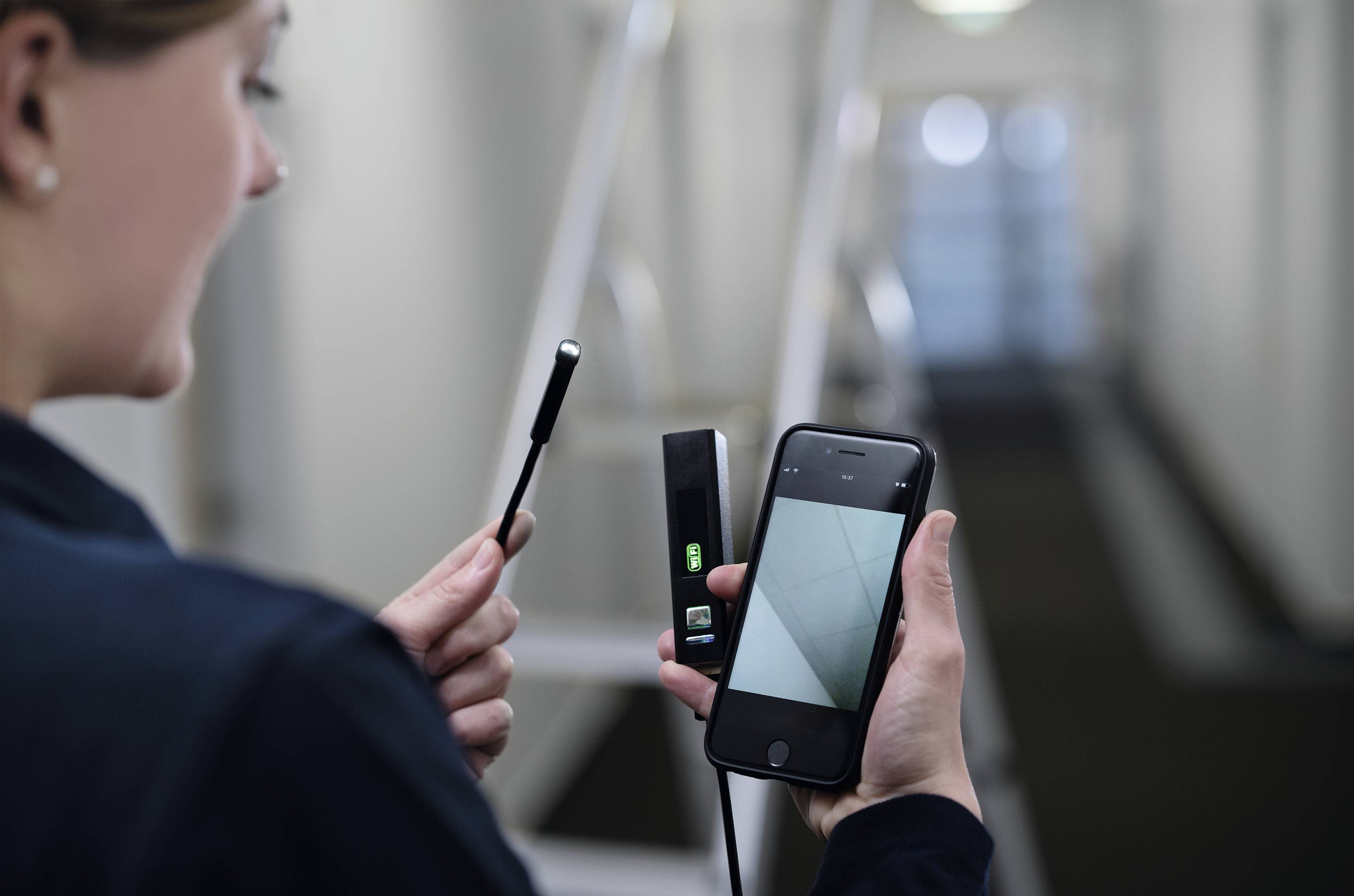 Une personne manipule un appareil portable avec un écran à côté d'un smartphone ; l'environnement est un couloir flou.