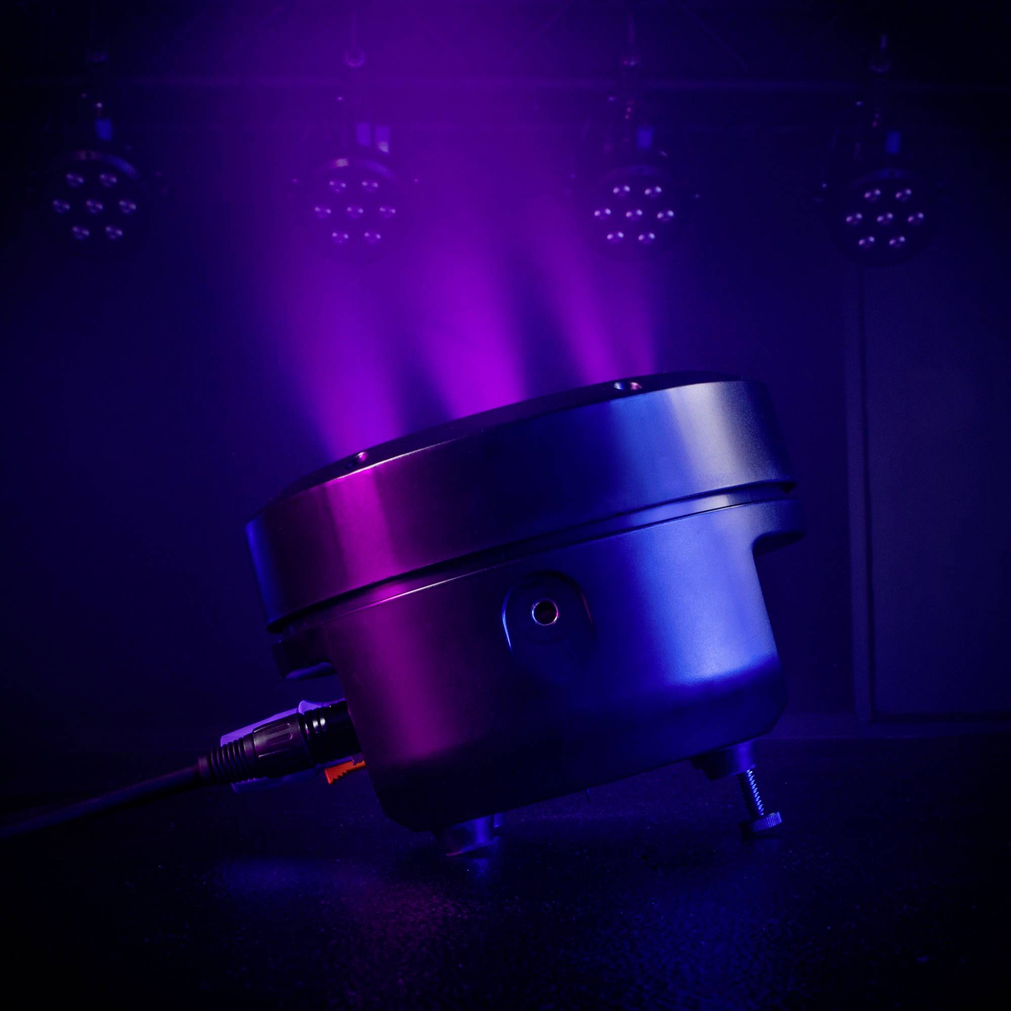 Un projecteur de scène noir projette de puissants effets de lumière colorés en bleu et violet sur une scène de théâtre sombre.