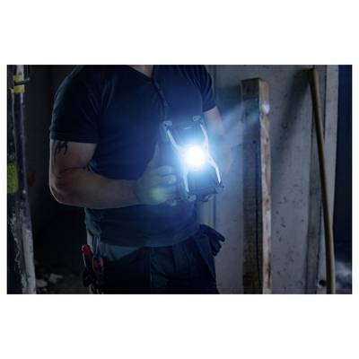 Travailleur dans un intérieur sombre tenant une lampe portative brillante ou un dispositif d'inspection, illuminant la zone devant lui.