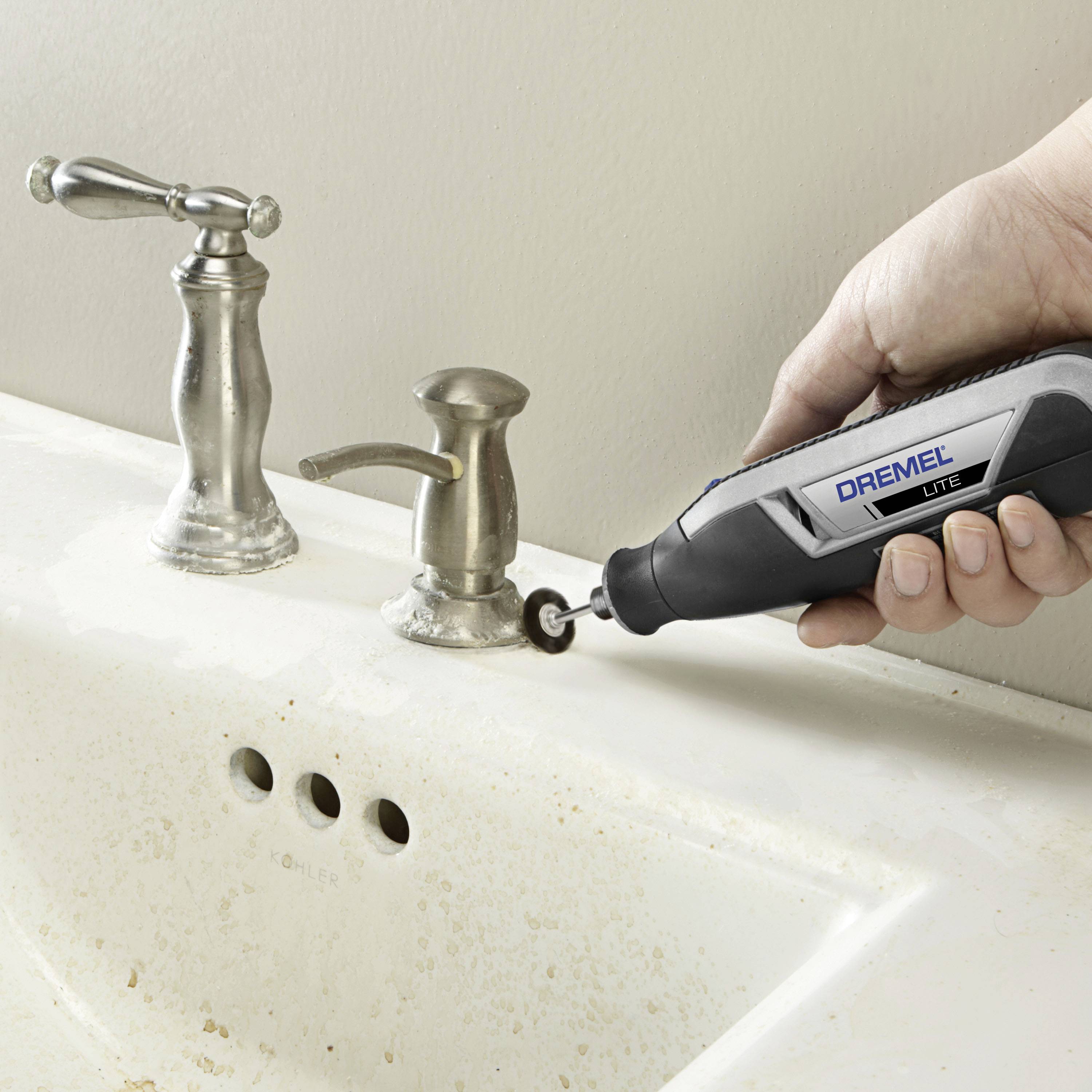 Une main tient un outil Dremel et lisse le bord d'un trou dans un lavabo blanc à côté d'un robinet.