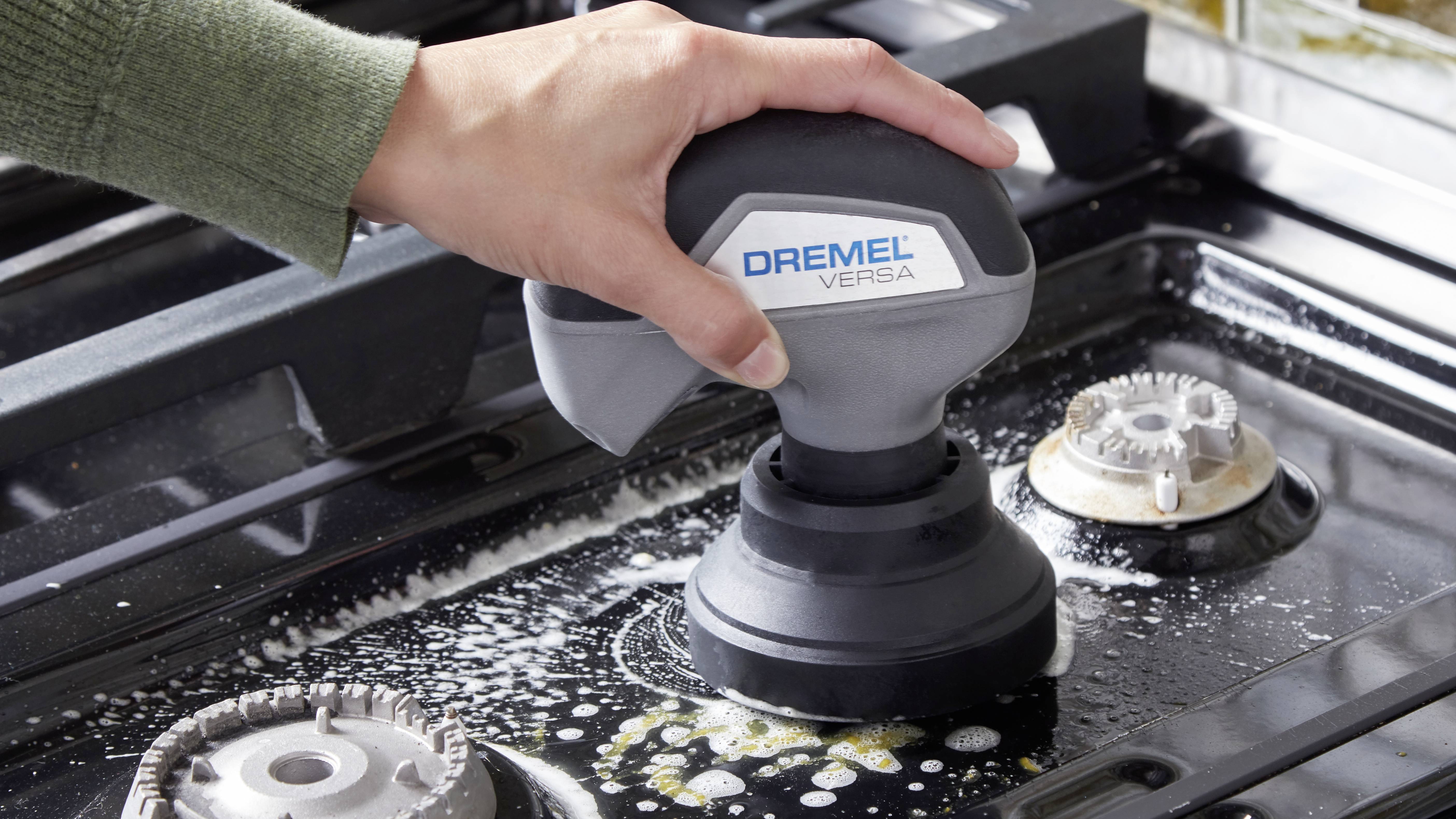 Une main nettoie une cuisinière à gaz avec un Dremel Versa. De l'eau mousseuse entoure l'appareil de nettoyage.