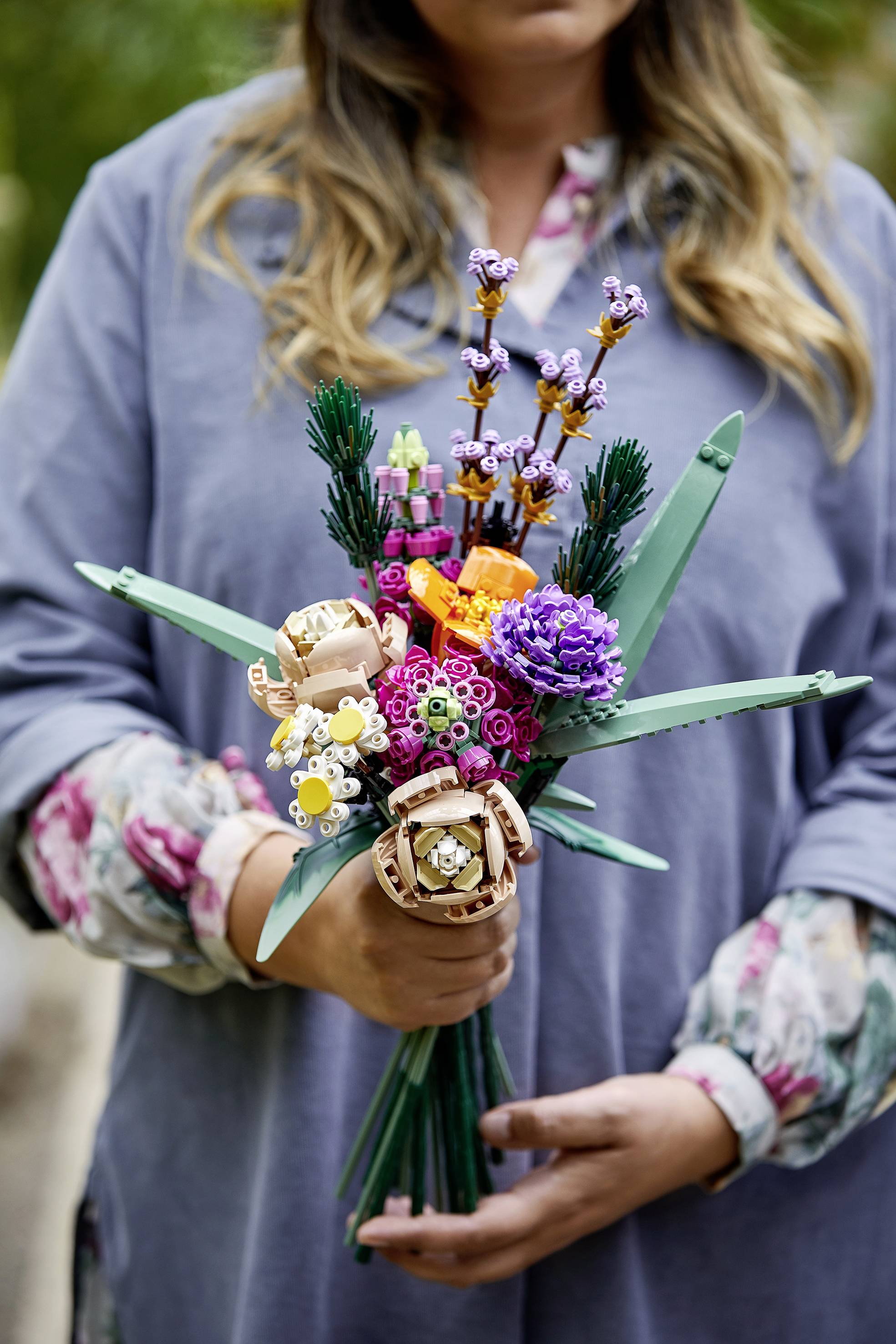 Une personne tient un bouquet fait de briques Lego, composé de fleurs colorées dans différentes couleurs et formes.