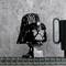 Un modèle LEGO d'un casque noir célèbre et un gobelet vert sont posés sur une étagère grillagée devant un mur gris.