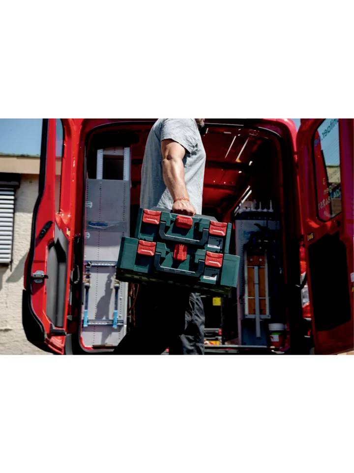 Une personne transporte une valise à outils verte vers un fourgon rouge. La porte arrière du véhicule est ouverte.