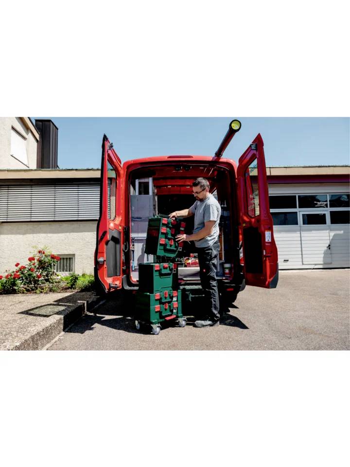 Un homme décharge une mallette à outils d'une camionnette rouge sur un site industriel.
