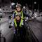 Une femme et un enfant, tous deux portant des casques, font du vélo ensemble le soir. Leurs gilets réfléchissants brillent dans l'obscurité.