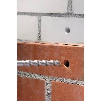 Un foret est dirigé vers un outil de brique rouge, tandis qu'un trou percé est visible dans un mur blanc en arrière-plan.