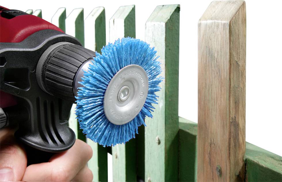 Une perceuse avec un accessoire de brosse bleu est utilisée pour nettoyer ou poncer la surface d'une clôture en bois verte.