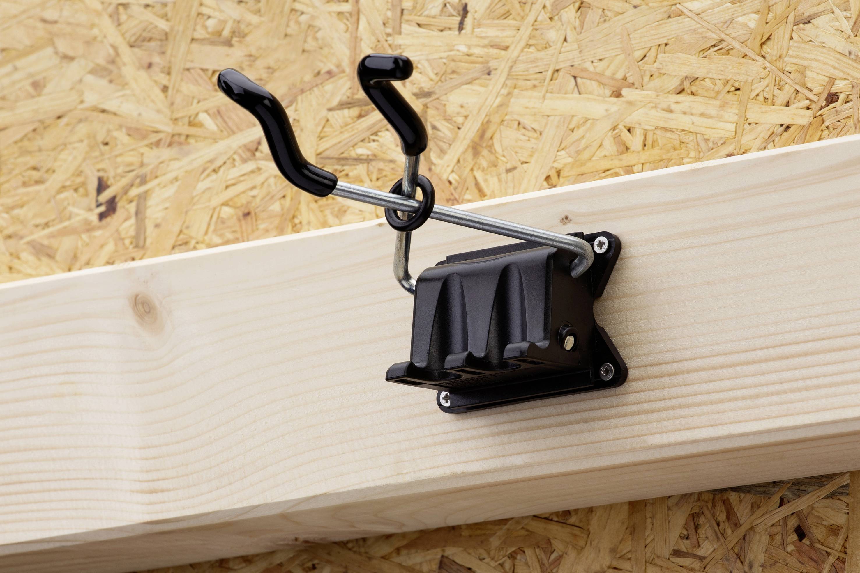 Support mural avec deux crochets noirs fixés sur une planche de bois, installé sur un mur en aggloméré. Adapté pour suspendre divers objets.
