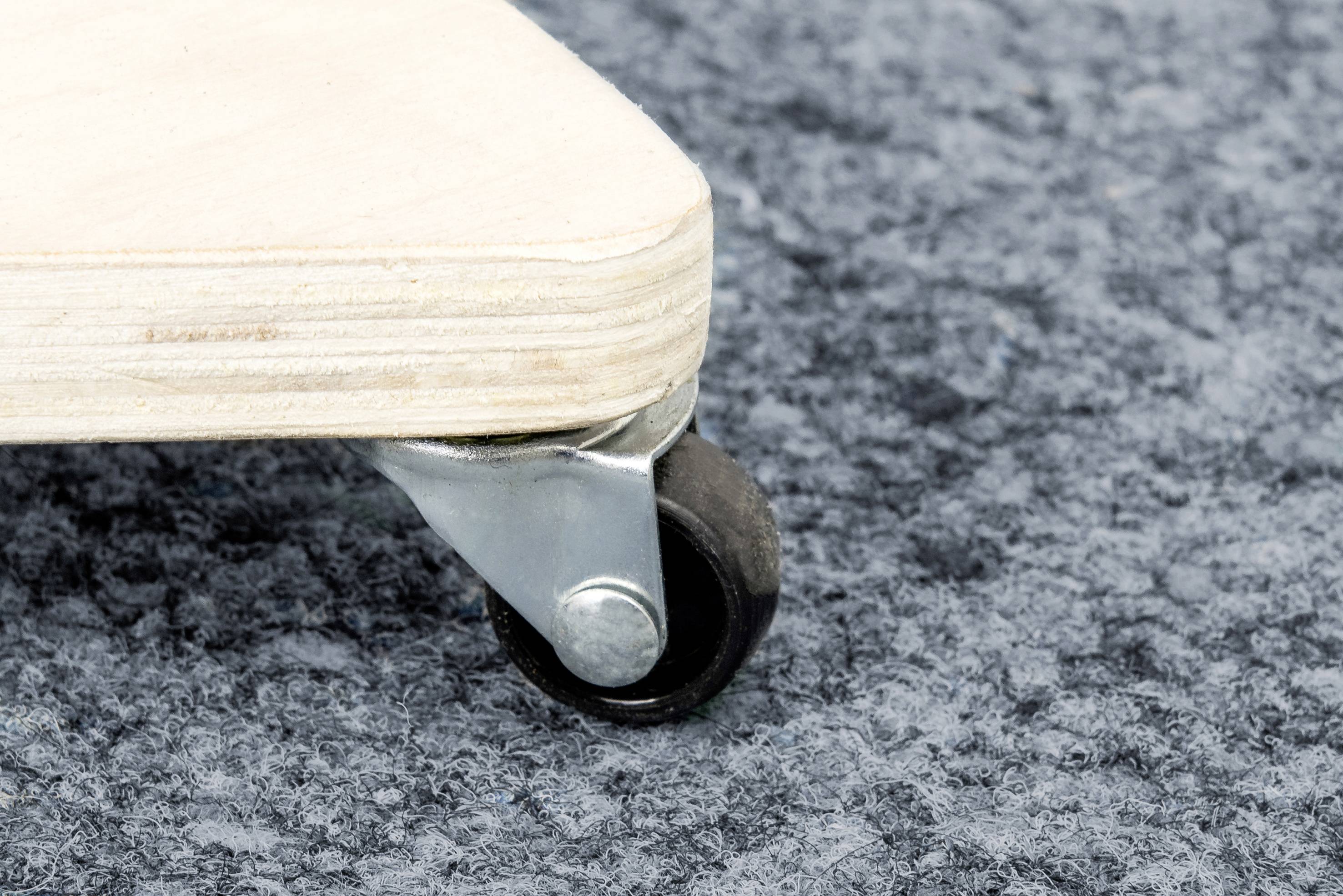 Une petite roue est montée à un coin d'une plaque. La plaque repose sur un revêtement de sol structuré gris.