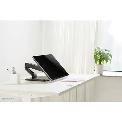 Un bureau moderne avec un écran sur un bras articulable, à côté un pot de crayons et une plante près de la fenêtre.