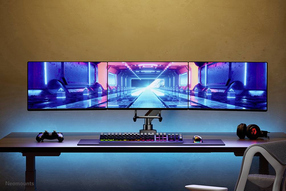 Trois écrans sur un bureau affichent une animation futuriste de tunnel. Un clavier et une manette sont posés en dessous. Configuration de jeu moderne.