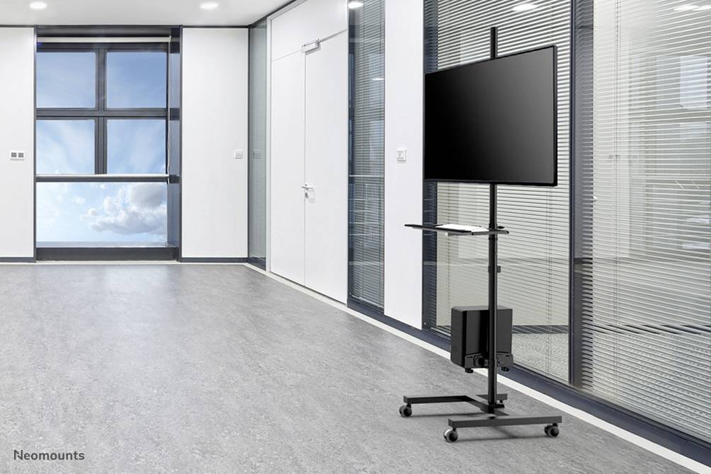 Une salle de conférence vide avec une grande fenêtre et un sol gris. Au premier plan, se trouve un support mobile pour moniteur avec un écran.