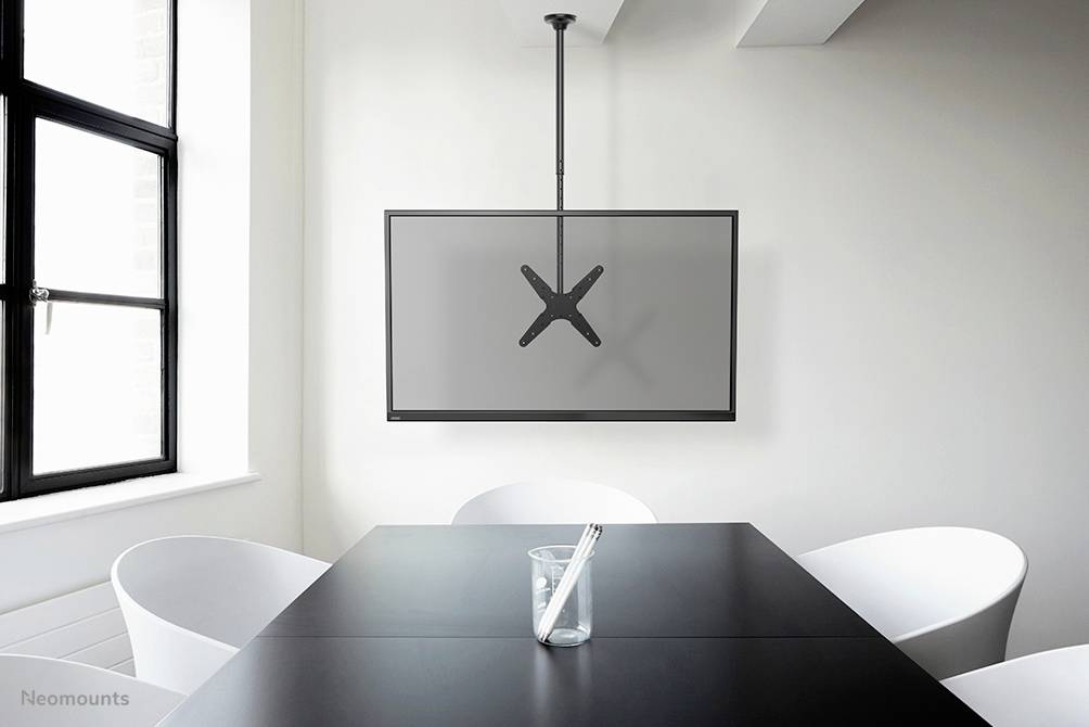 Une salle de réunion minimaliste avec une table, quatre chaises blanches et un écran plat monté au plafond.