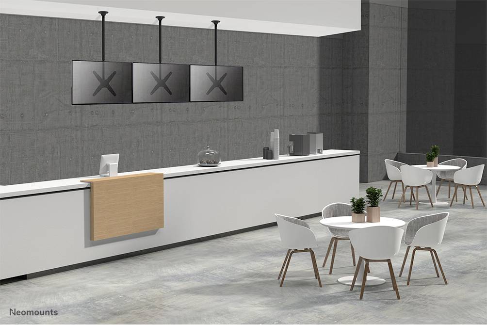 Un espace café moderne avec un long comptoir équipé d'écrans. Au premier plan, des tables rondes sont disposées avec des chaises blanches.