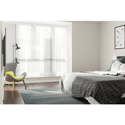 Une chambre moderne avec une grande fenêtre, une housse de lit grise, un fauteuil à côté d'un lampadaire et un tableau accroché au mur.